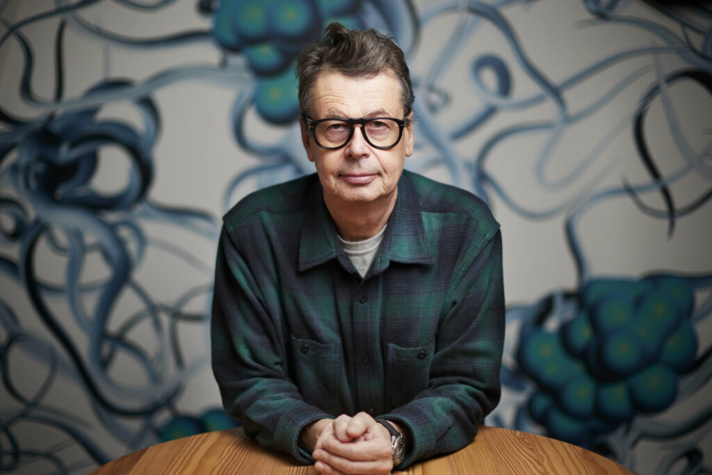 Das Foto zeigt ein Portrait des Künstlers Peter Kogler im Weinkeller des Arthotel Lasserhaus in Brixen. Im Hintergrund sieht man sein Kunstwerk "ohne Titel, 2023"