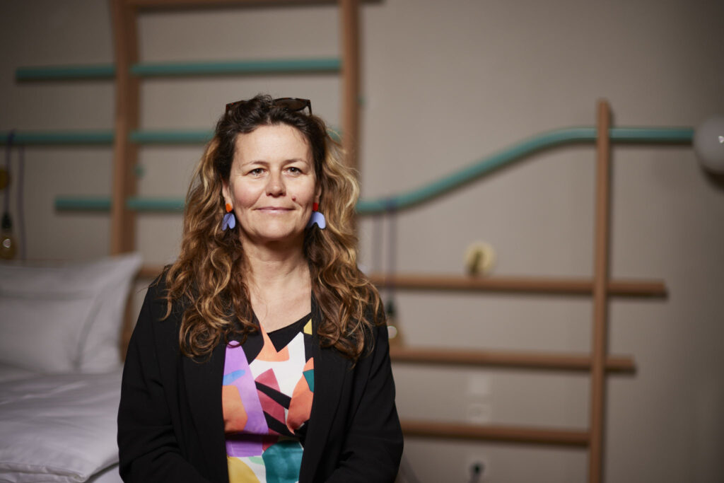 Das Bild zeigt Ingrid Hora vor ihrem Kunstwerk "Sprossenwand, 2023", welches in einem der Künstlerzimmer im Erdgeschoss des Lasserhaus ausgestellt ist.