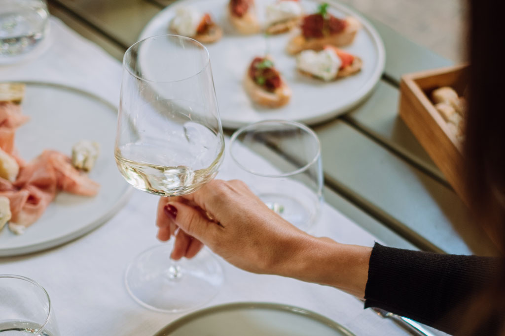 Das Bild zeigt eine weibliche Hand mit einem Glas Weisswein